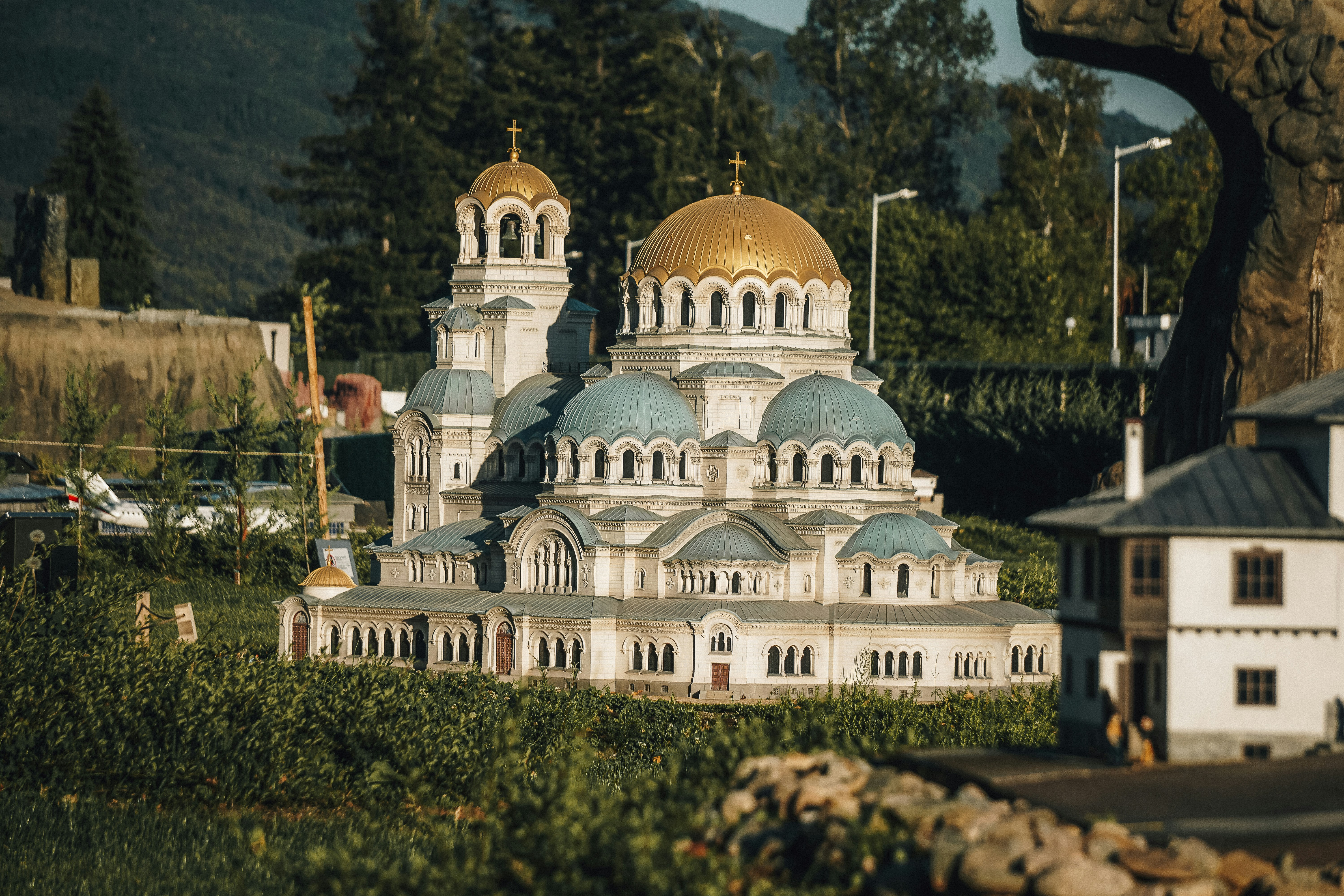 Ornate cathedral with golden and blue domes in greenery.
