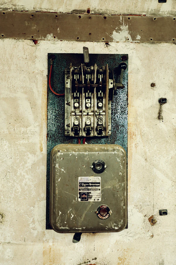 An old breaker box and knife switch mounted on a scuffed whitewashed wall