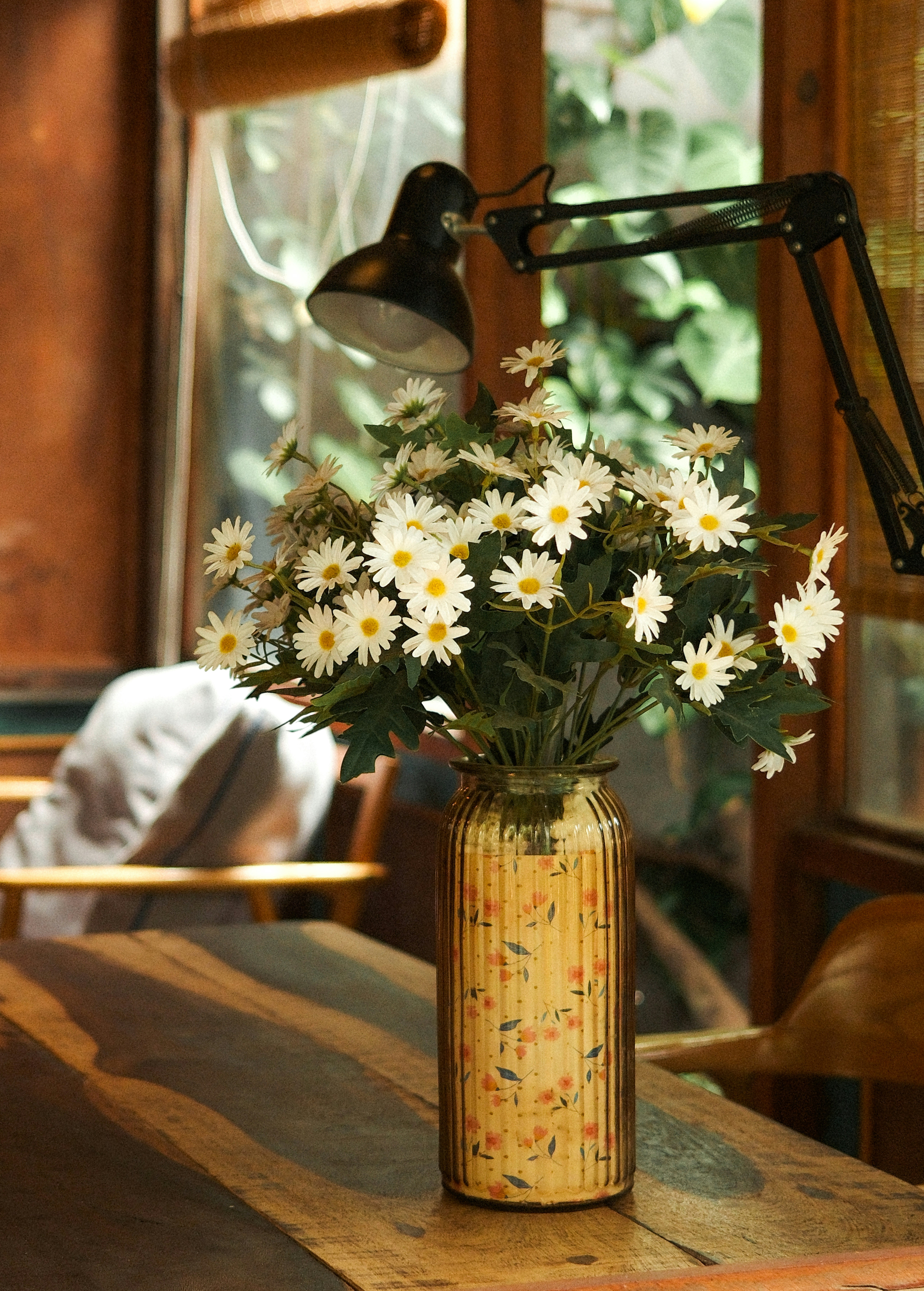Margaridas brancas em um vaso decorativo em uma mesa.