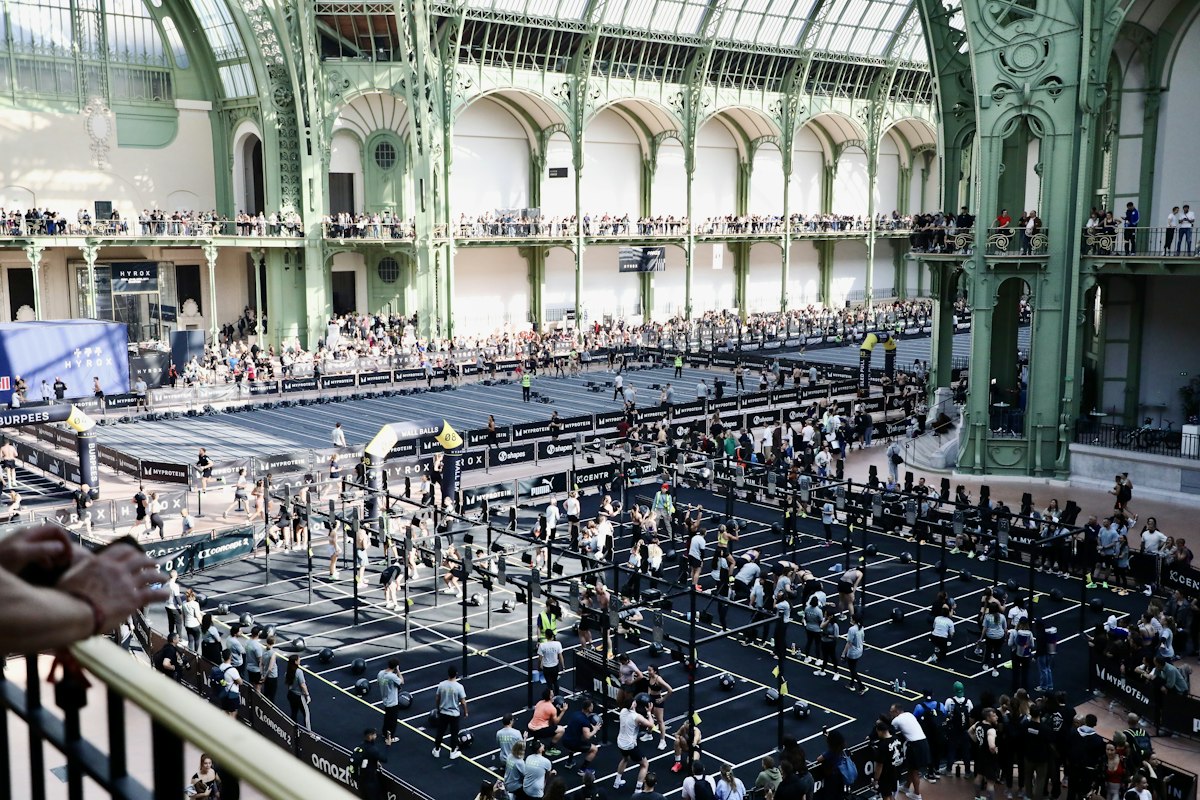 Vue en plongée d'un grand hall sous verrière où des centaines d'athlètes enchaînent les stations d'une course de fitness