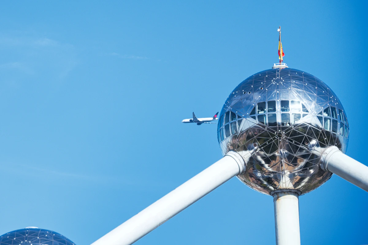 Airplane flying past the Atomium structure under clear blue sky