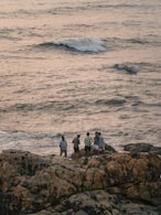 Group of people standing on rocks by the sea.