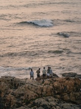 Group of people standing on rocks by the sea.