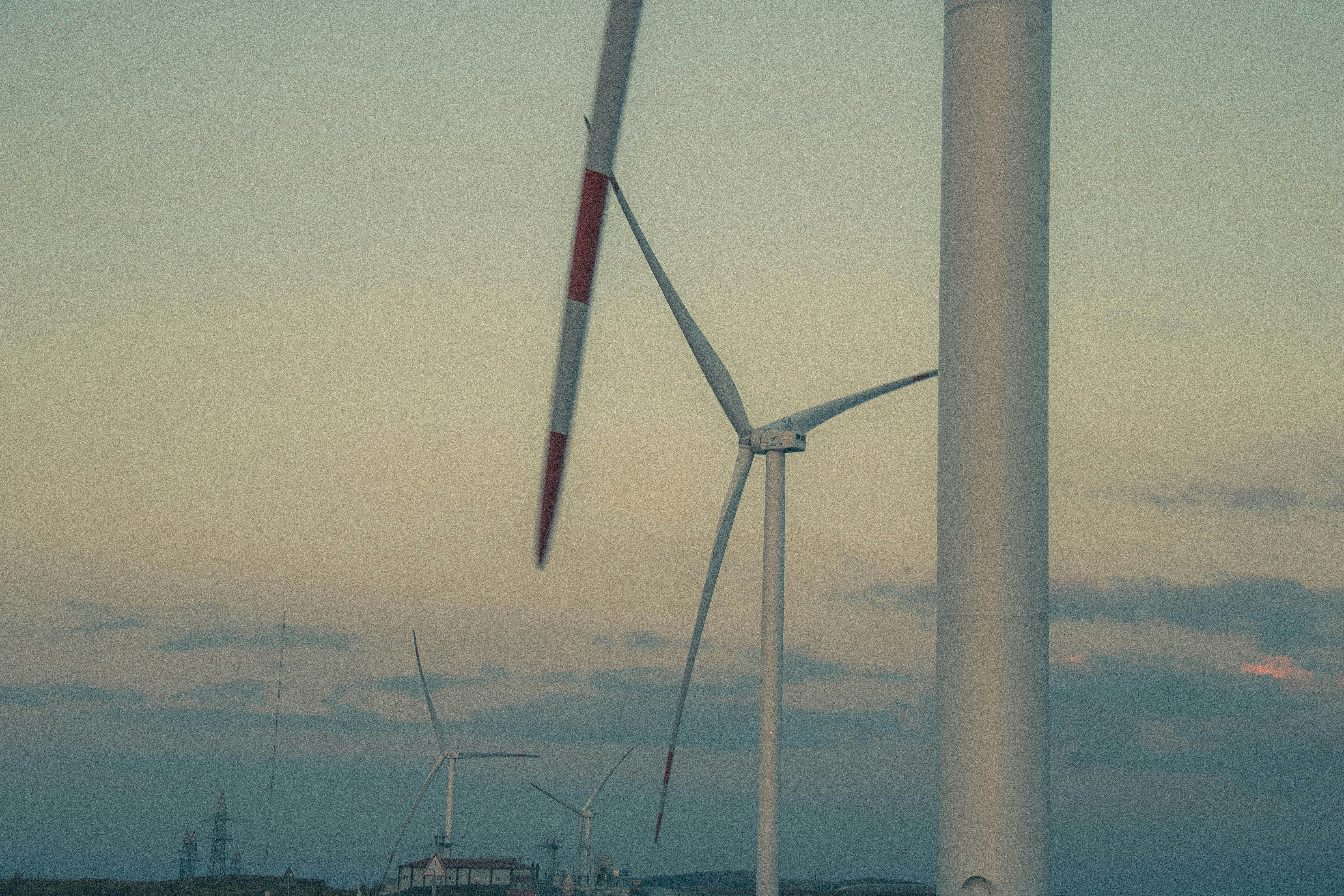 Wind turbines stand against a pale sky at dusk.
