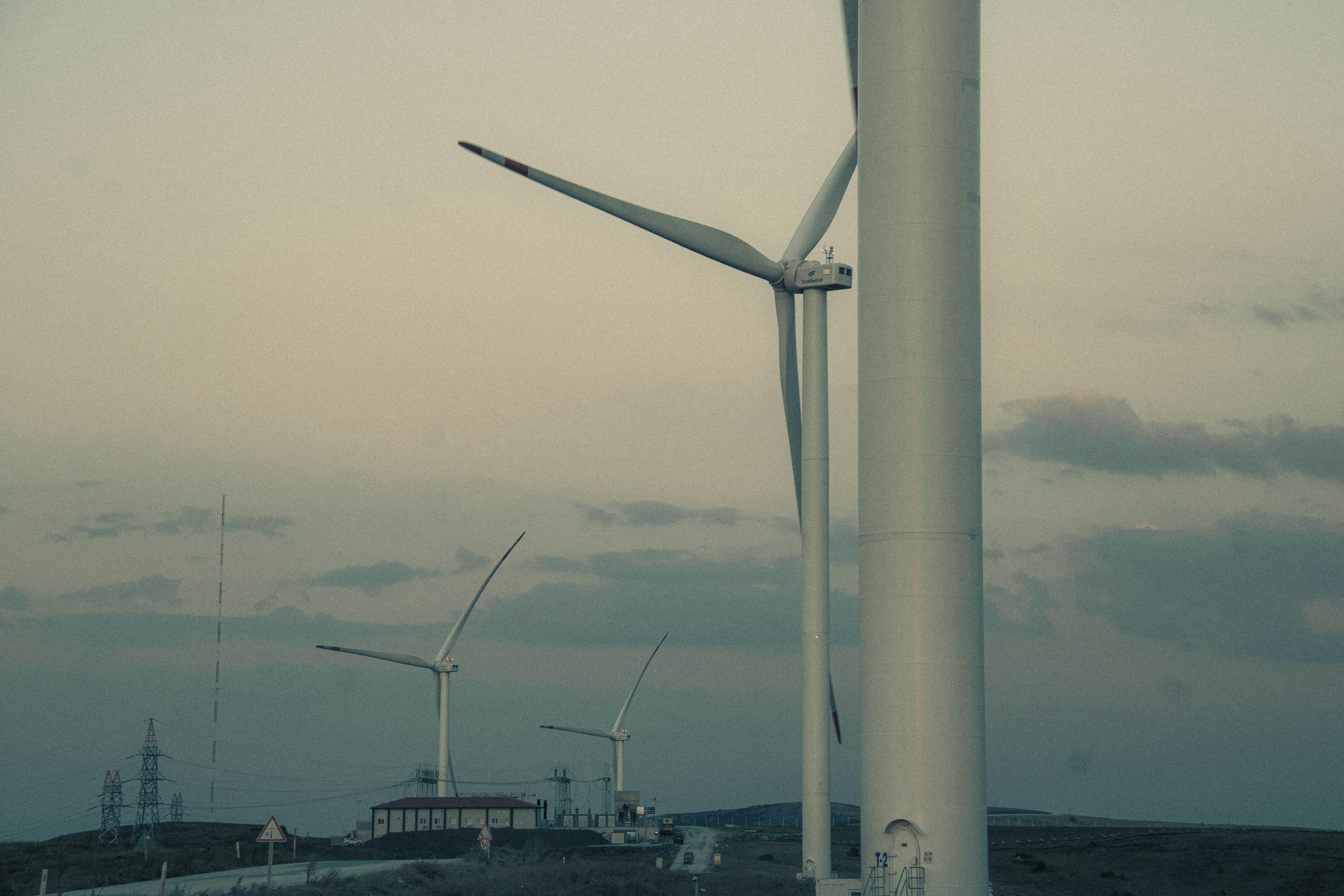 Wind turbines stand on a grassy hill under a cloudy sky.