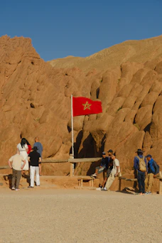 Moroccan flag flies over tourists in desert landscape