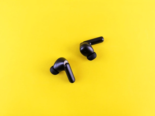 Two black wireless earbuds on a yellow background