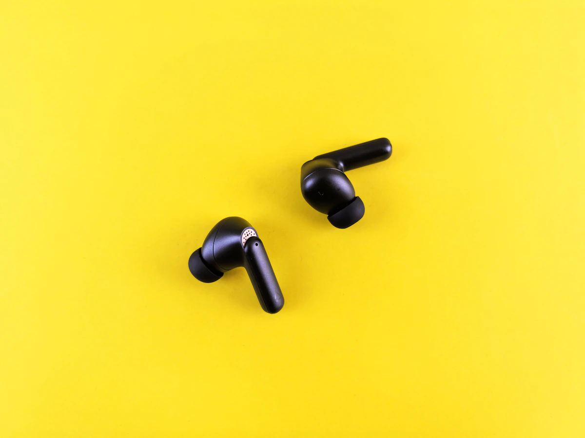 Pair of black wireless earbuds on a yellow background