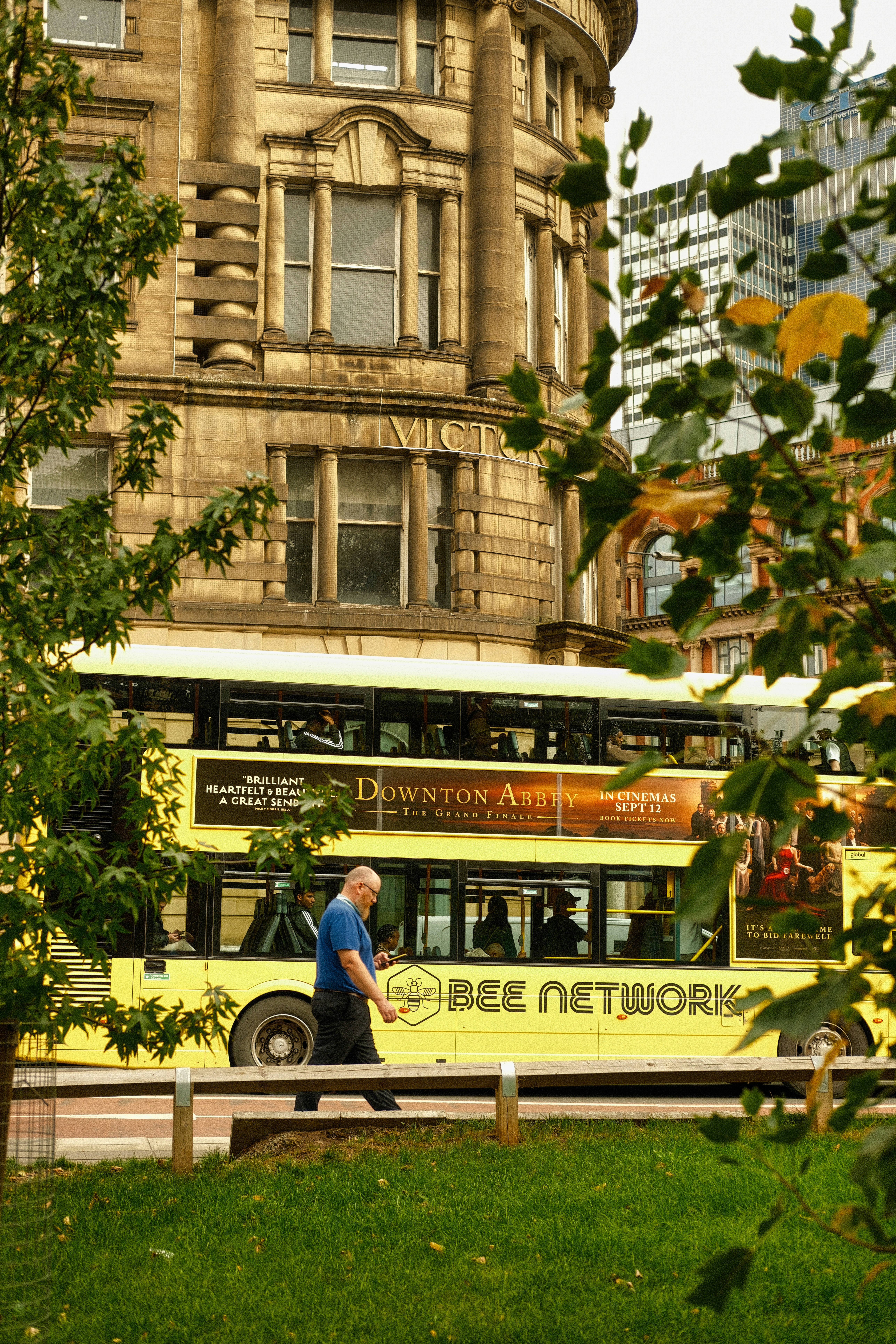 Man walks past a yellow double-decker bus in city.