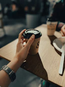 Hand holding a disposable coffee cup on a wooden table.