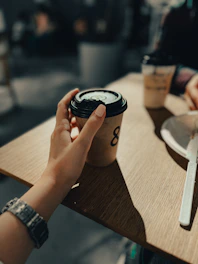 Hand holding a disposable coffee cup on a wooden table.