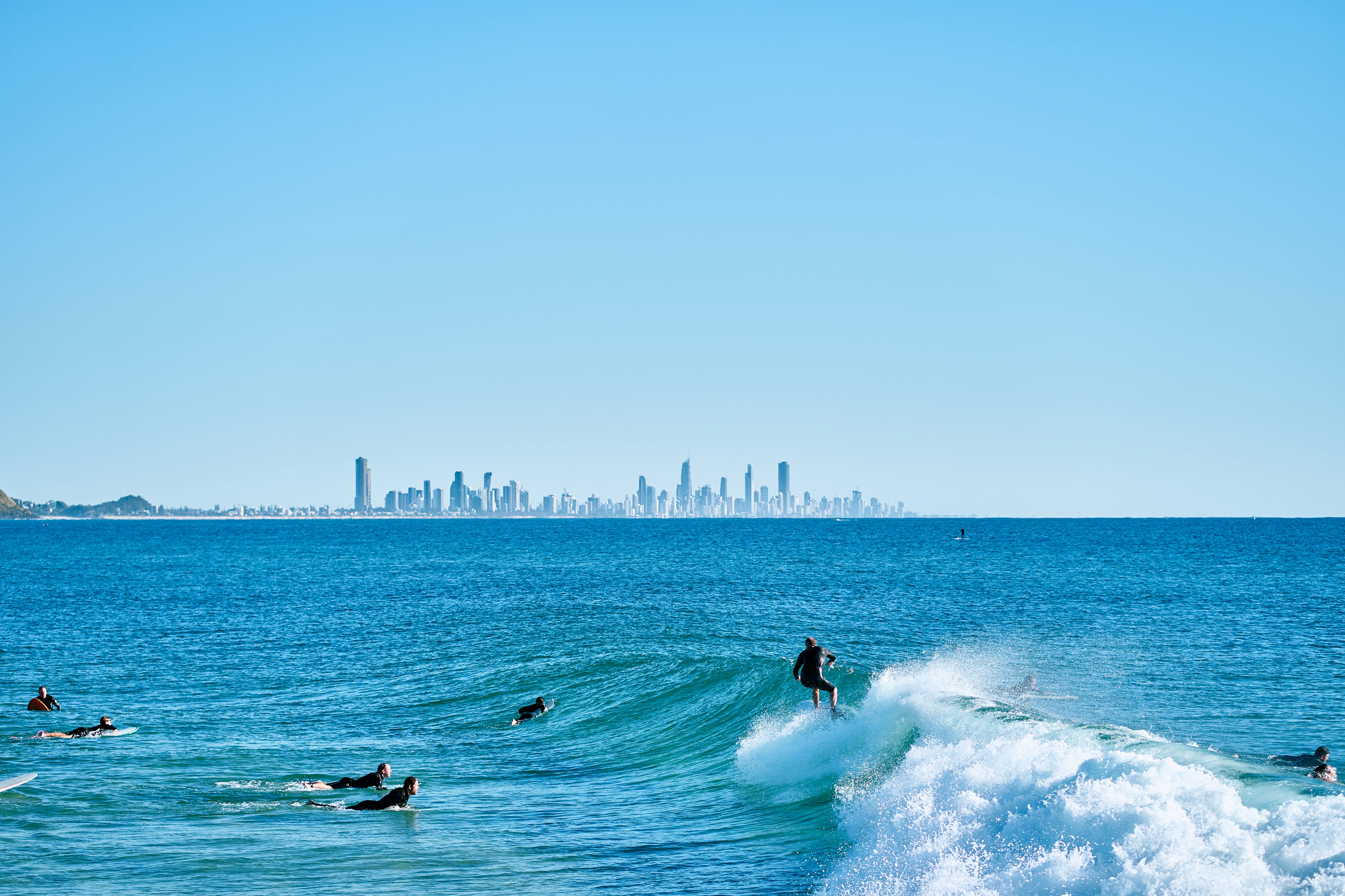 Surfers ride waves with a city skyline in the distance