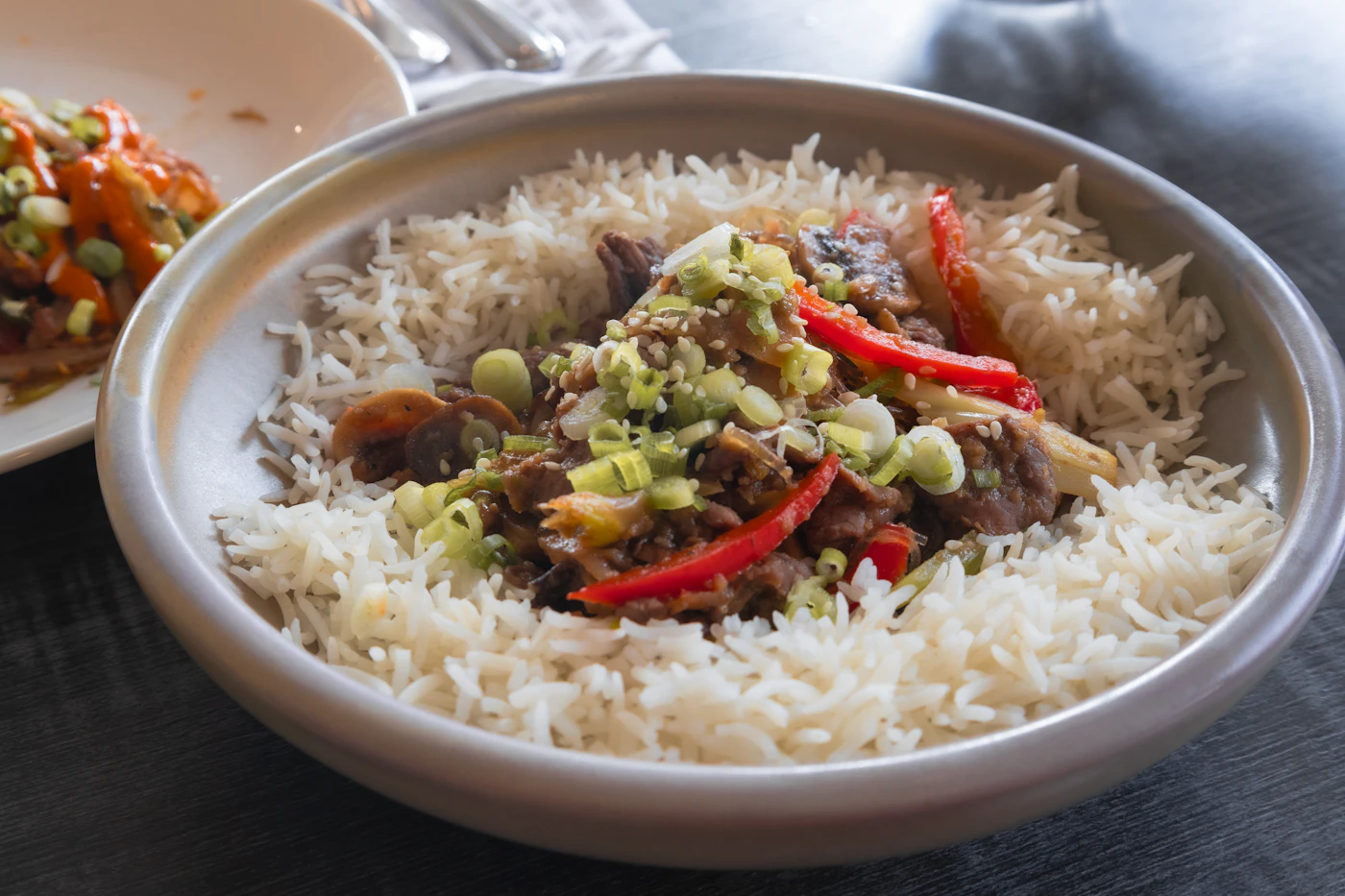 Rice bowl topped with browned beef, peppers, scallions, and fresh herbs