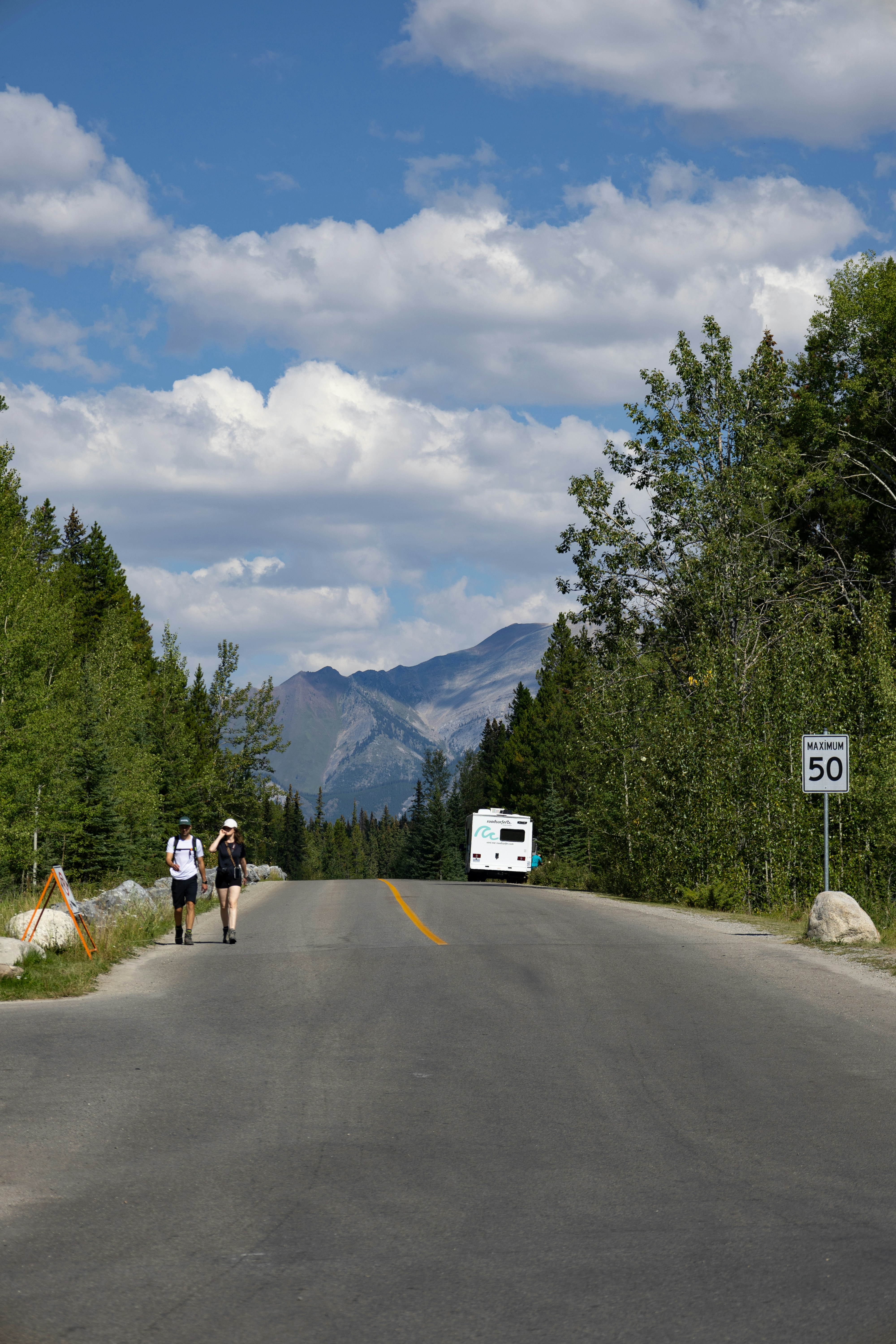 Two hikers walk down a road towards mountains