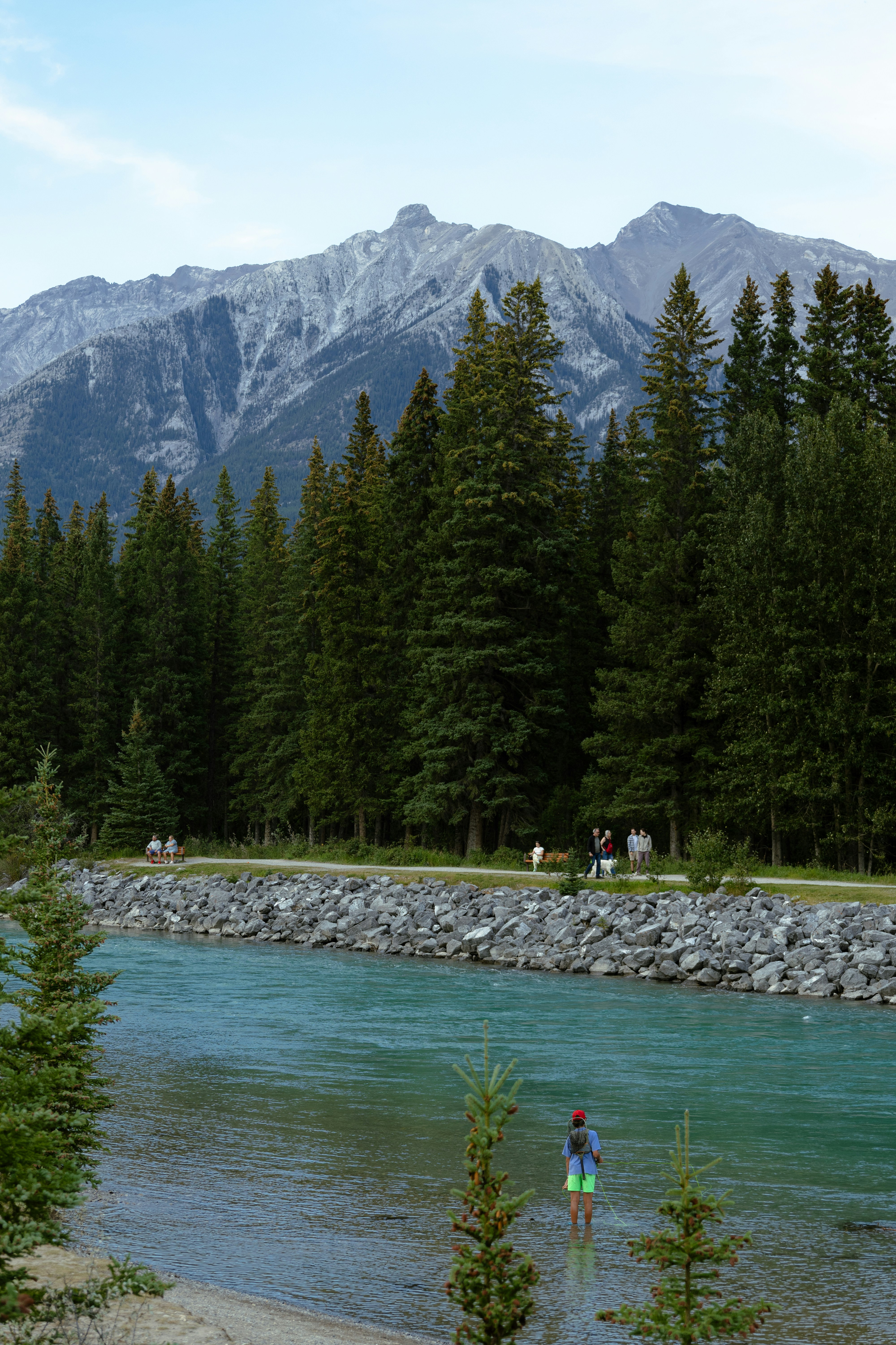 People walk along a path beside a river and forest.