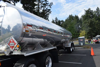 Shiny tanker truck with hazard symbols parked outdoors.