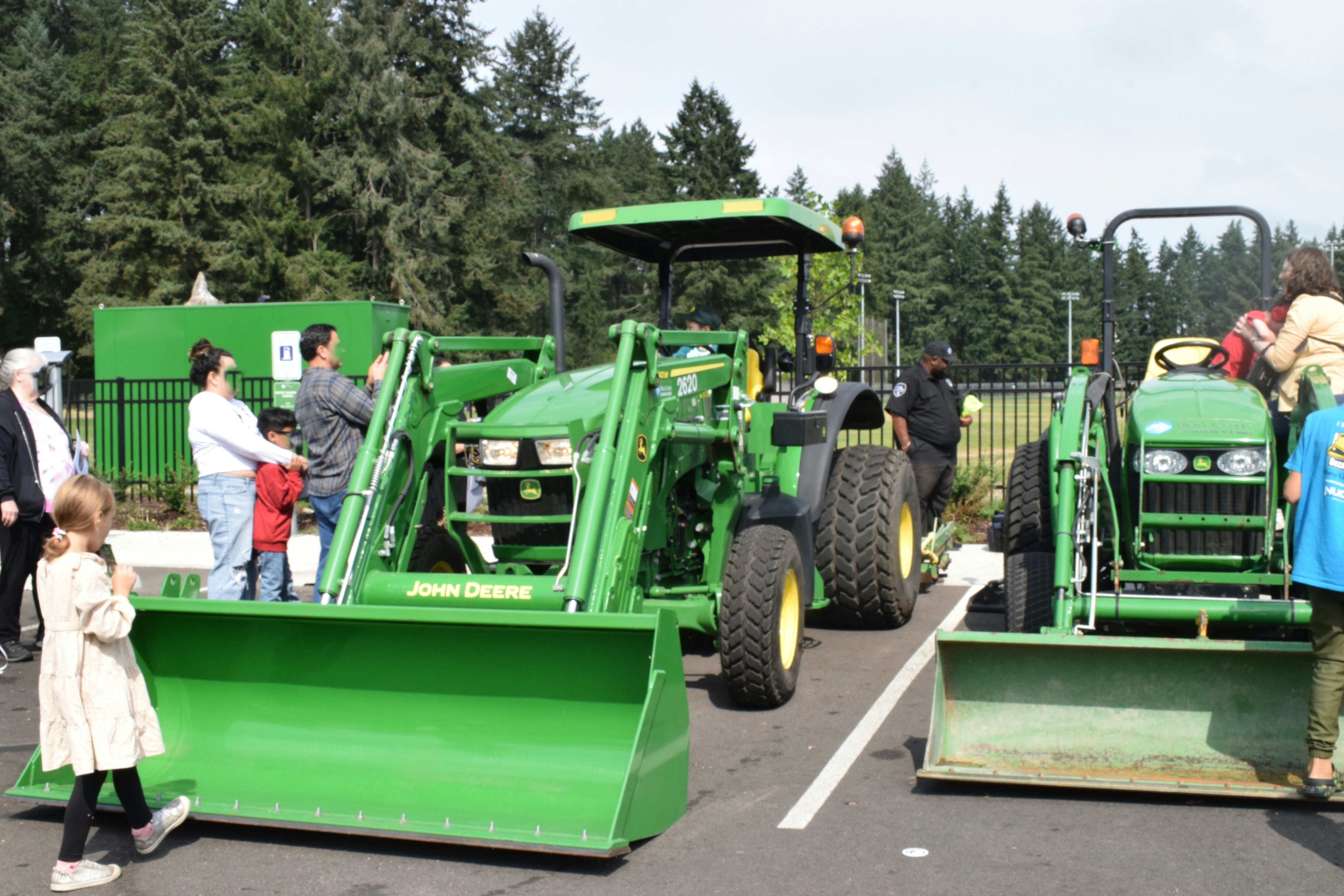 People gather around two green john deere tractors.