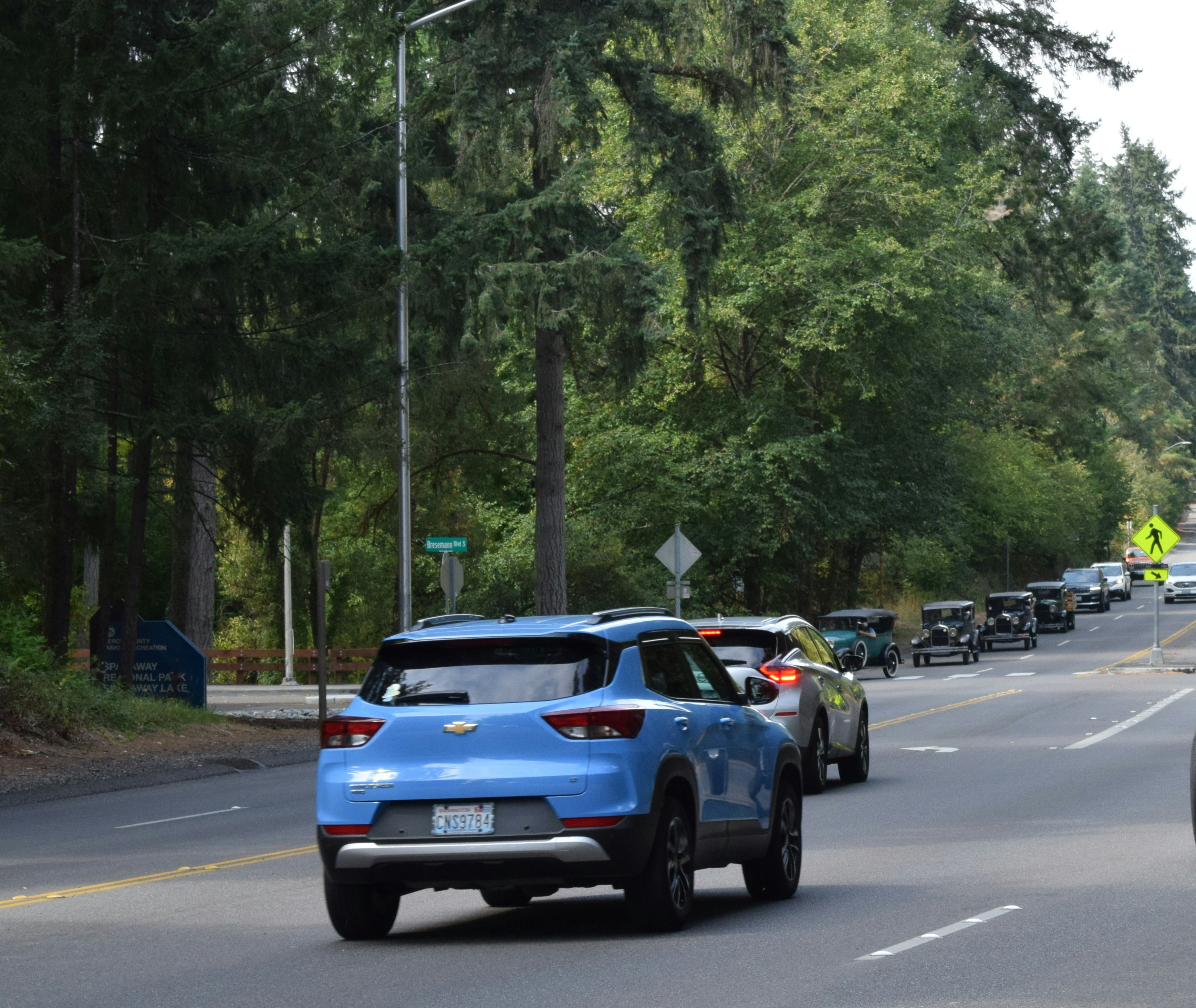 Blue car leads a line of vehicles on a road.
