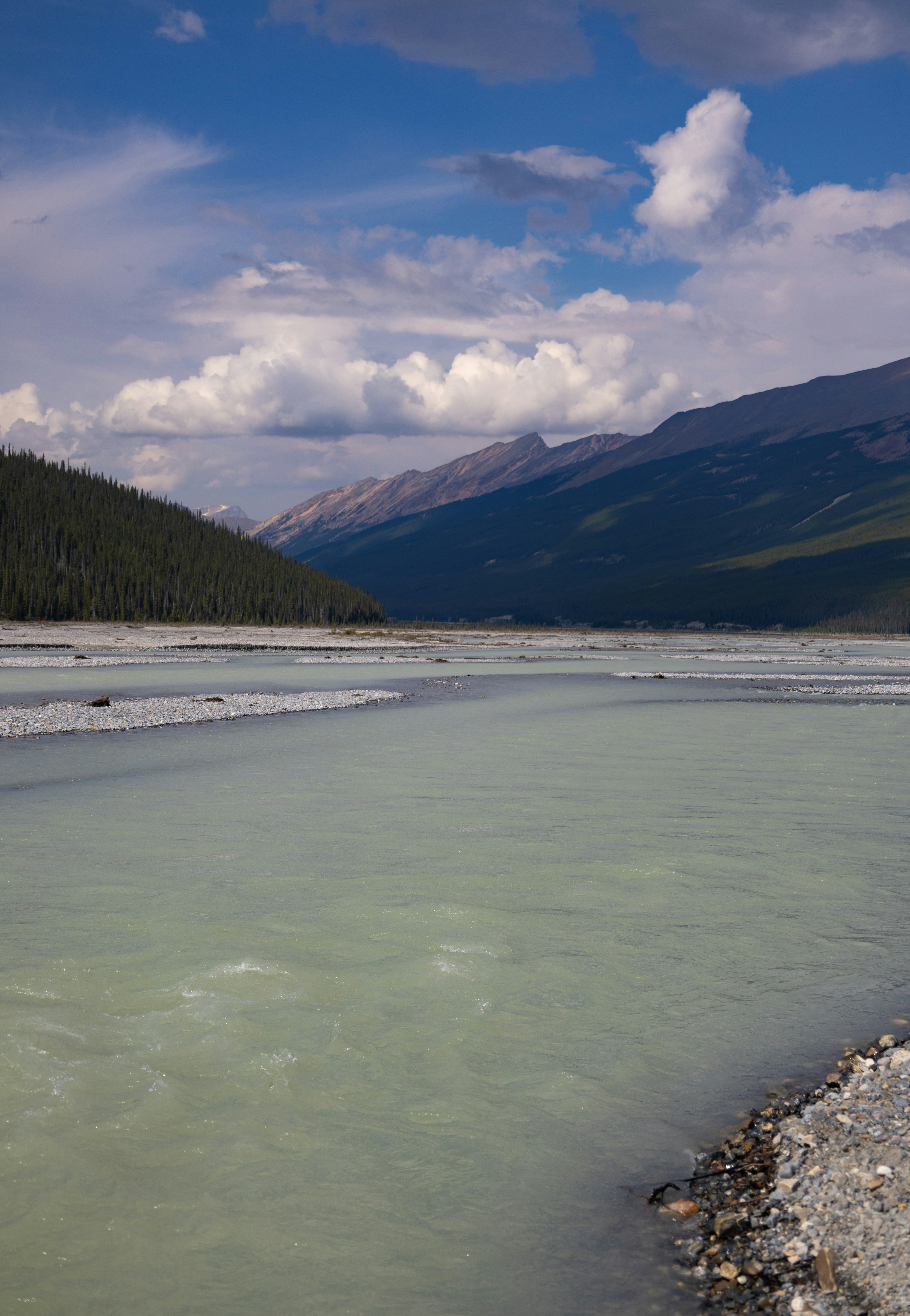 A wide glacial river flows through a valley with mountains.