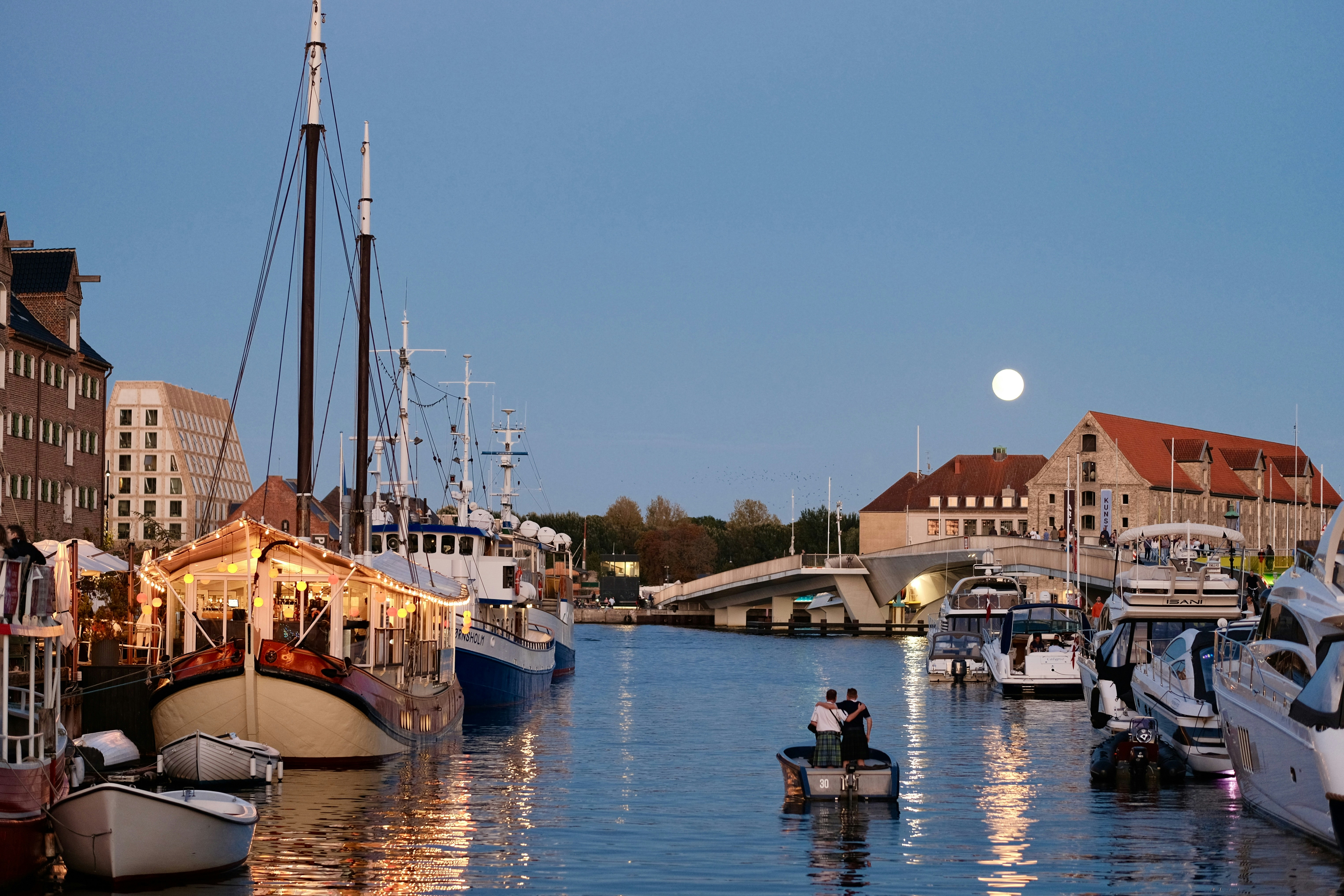 Boats docked in a canal with buildings and a full moon.