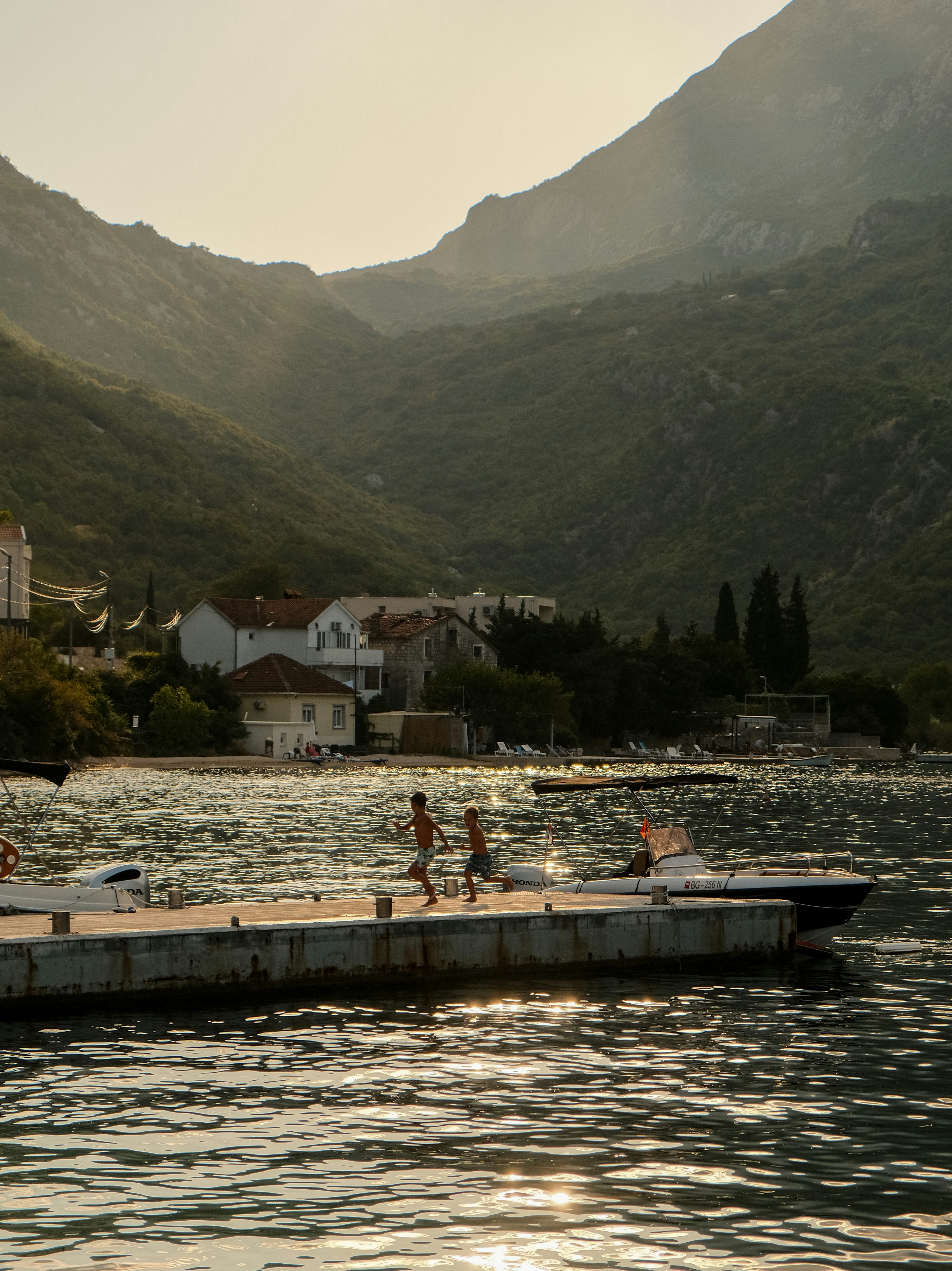 Two people run along a pier near a coastal village.