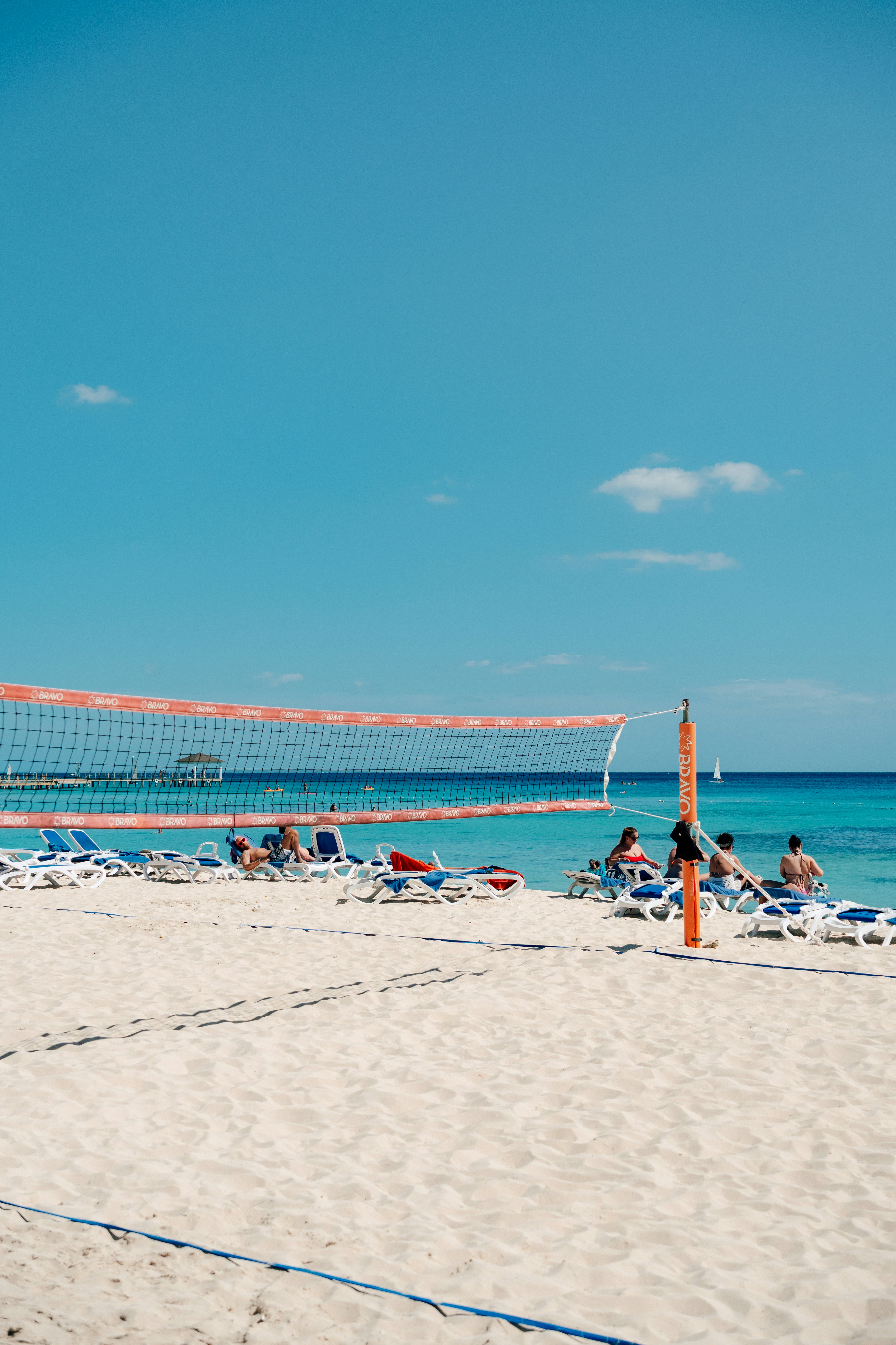 Volleyball net on a sandy beach with people relaxing.