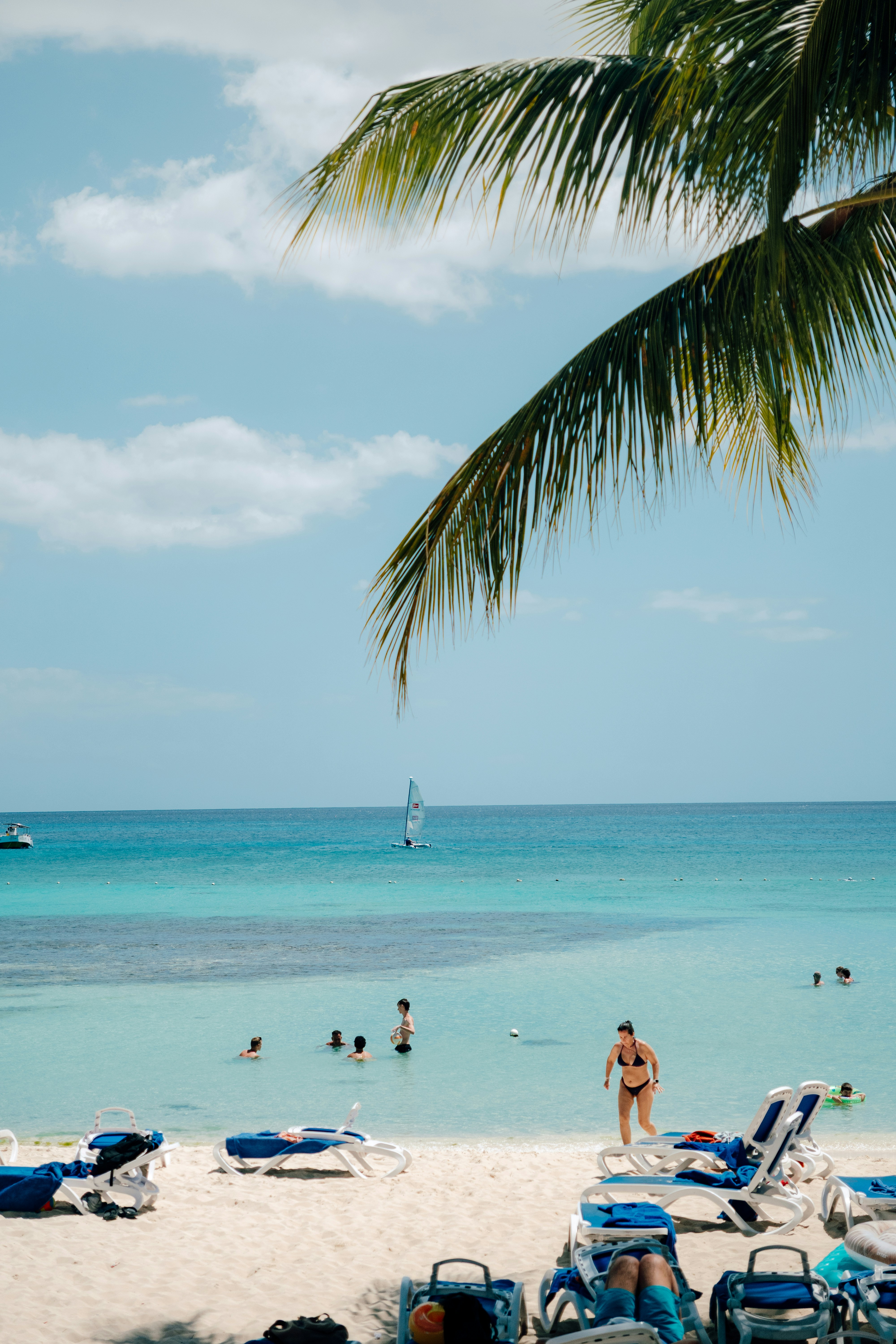People swimming in clear turquoise ocean water near beach chairs.
