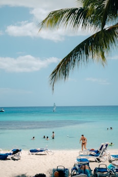 People swimming in clear turquoise ocean water near beach chairs.