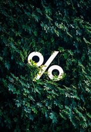 A white percentage sign logo surrounded by green leaves.