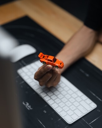Hand holding a small orange toy car over keyboard