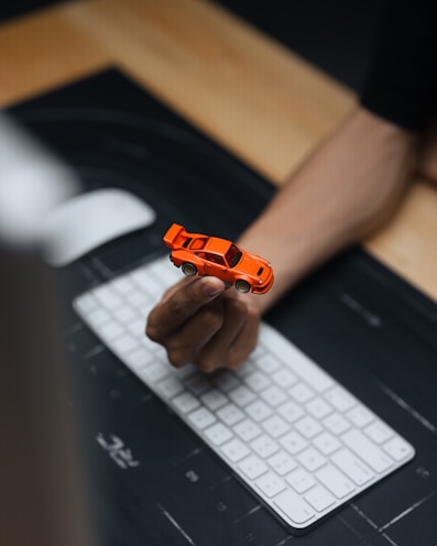 Hand holding a small orange toy car over keyboard