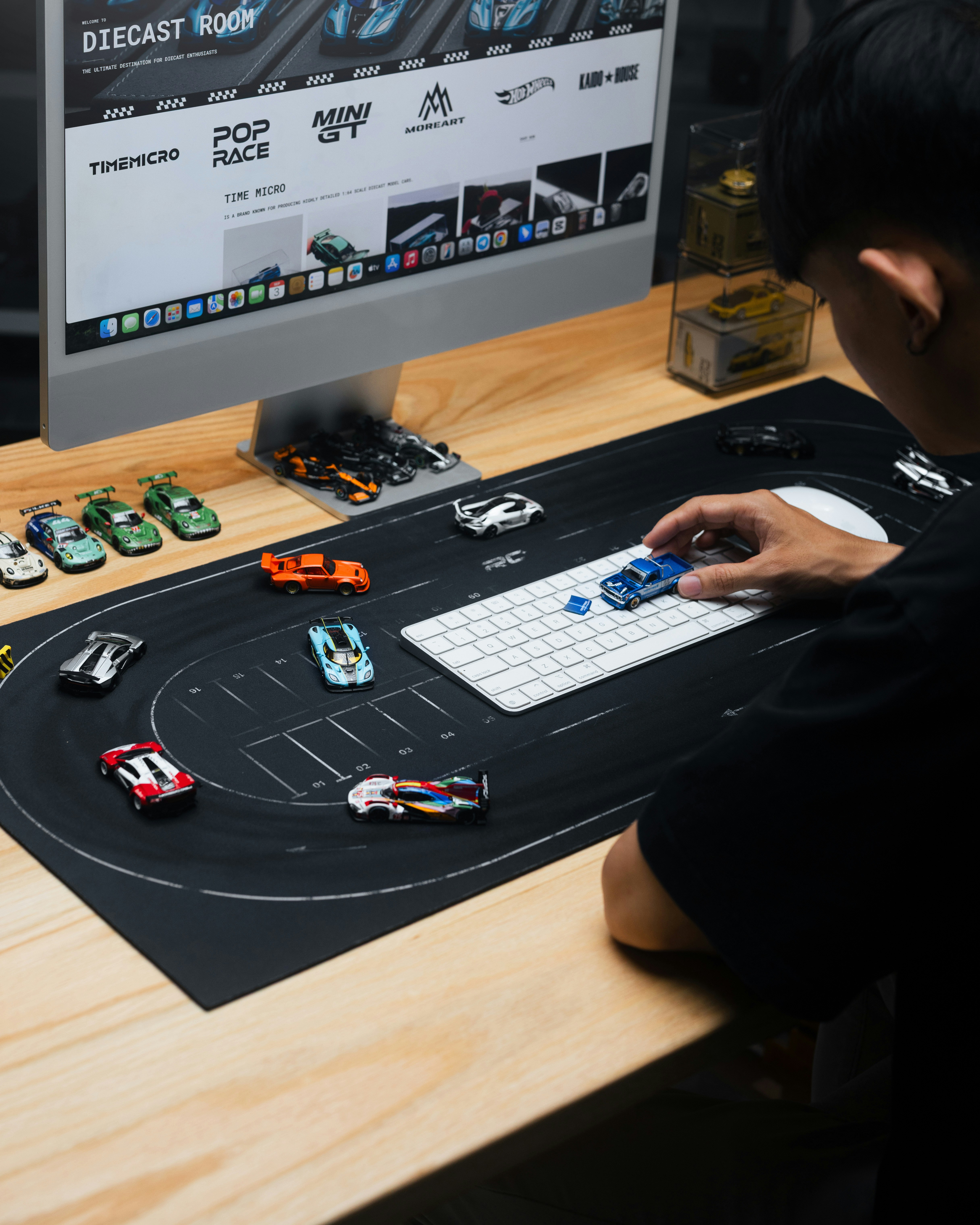Person arranging toy cars on a race track mat.