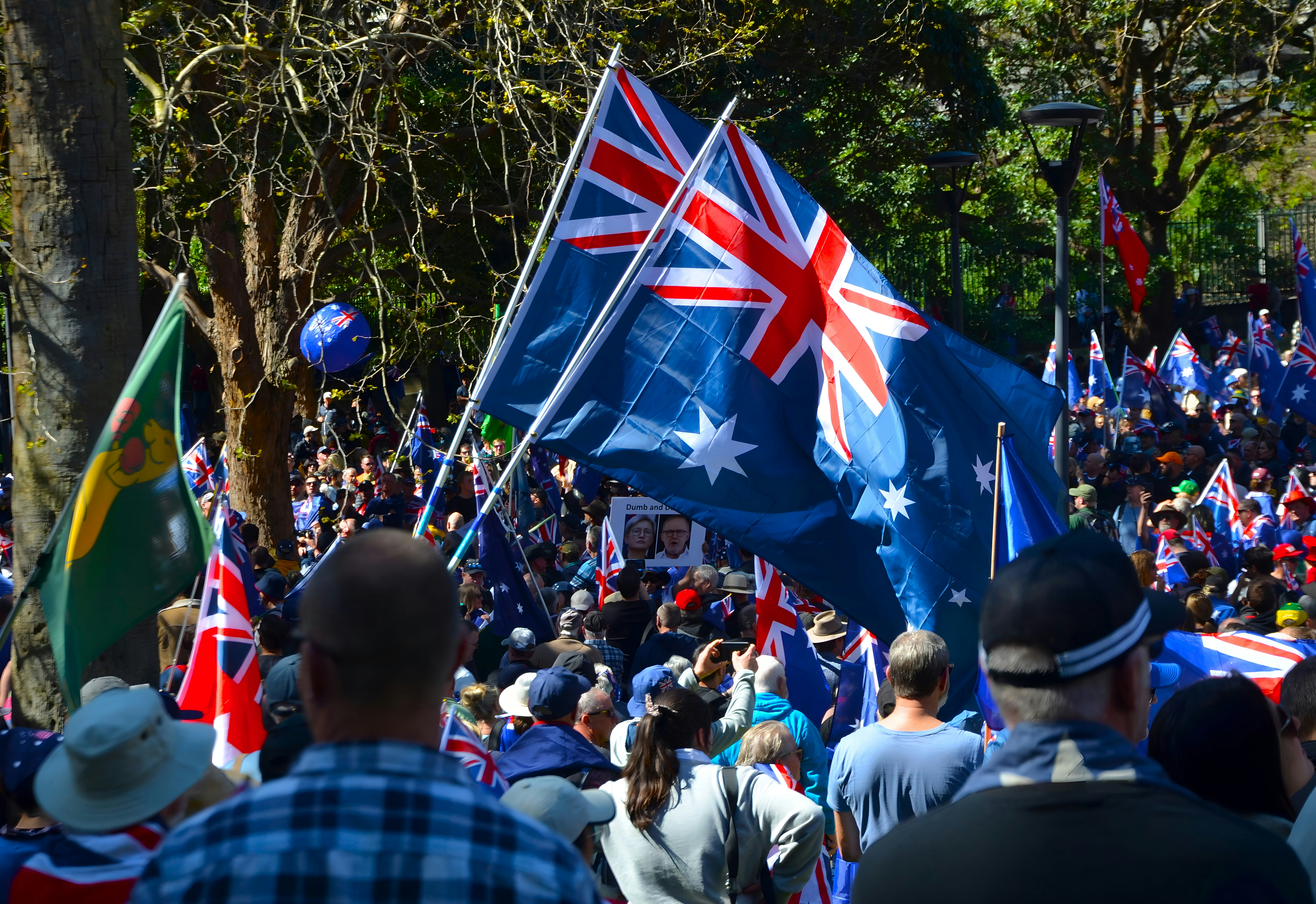 Crowd holding australian flags at a sunny outdoor event