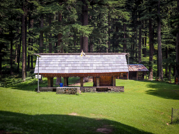 Wooden structure with stone foundation in a grassy clearing.
