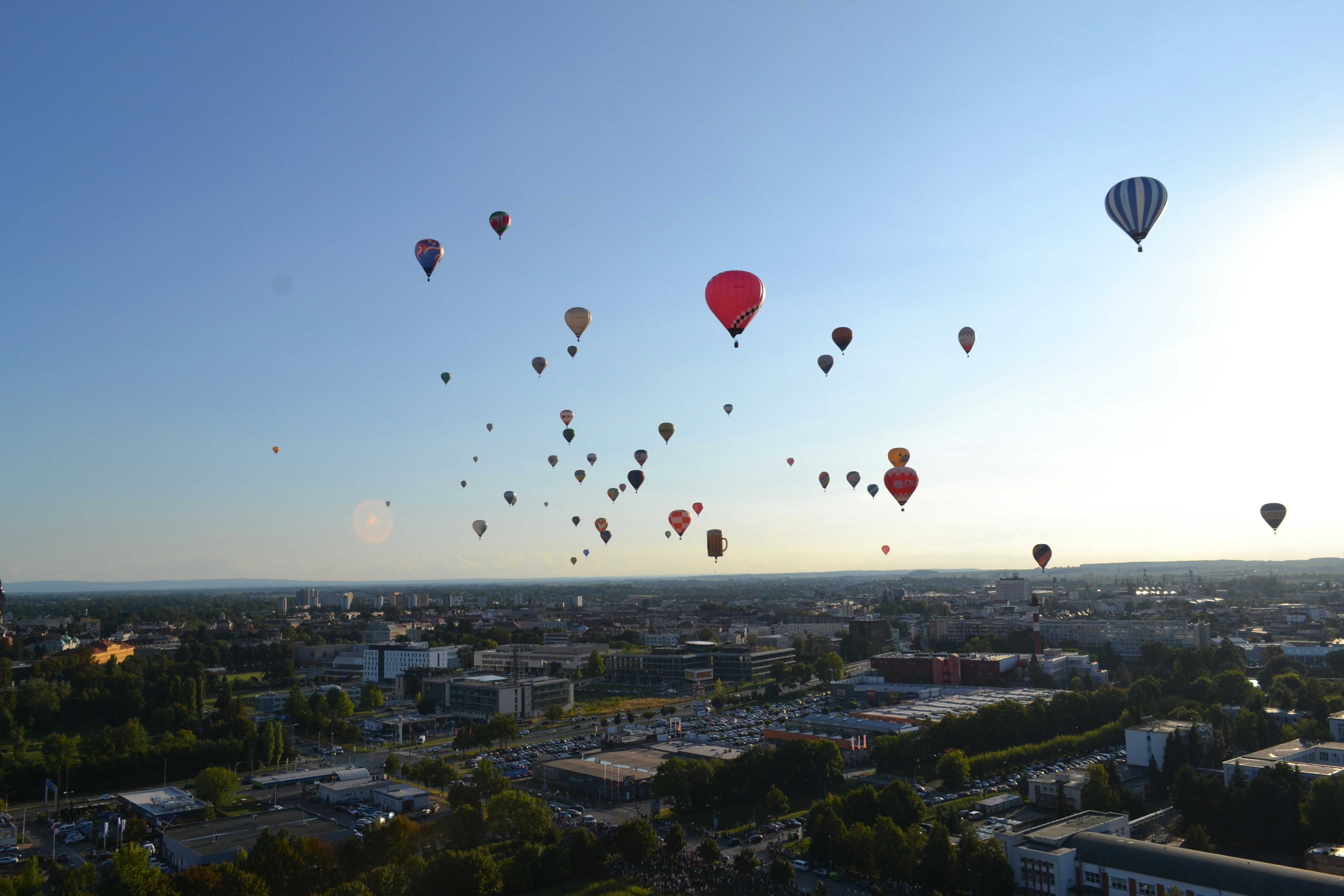 Many hot air balloons float over a city skyline.