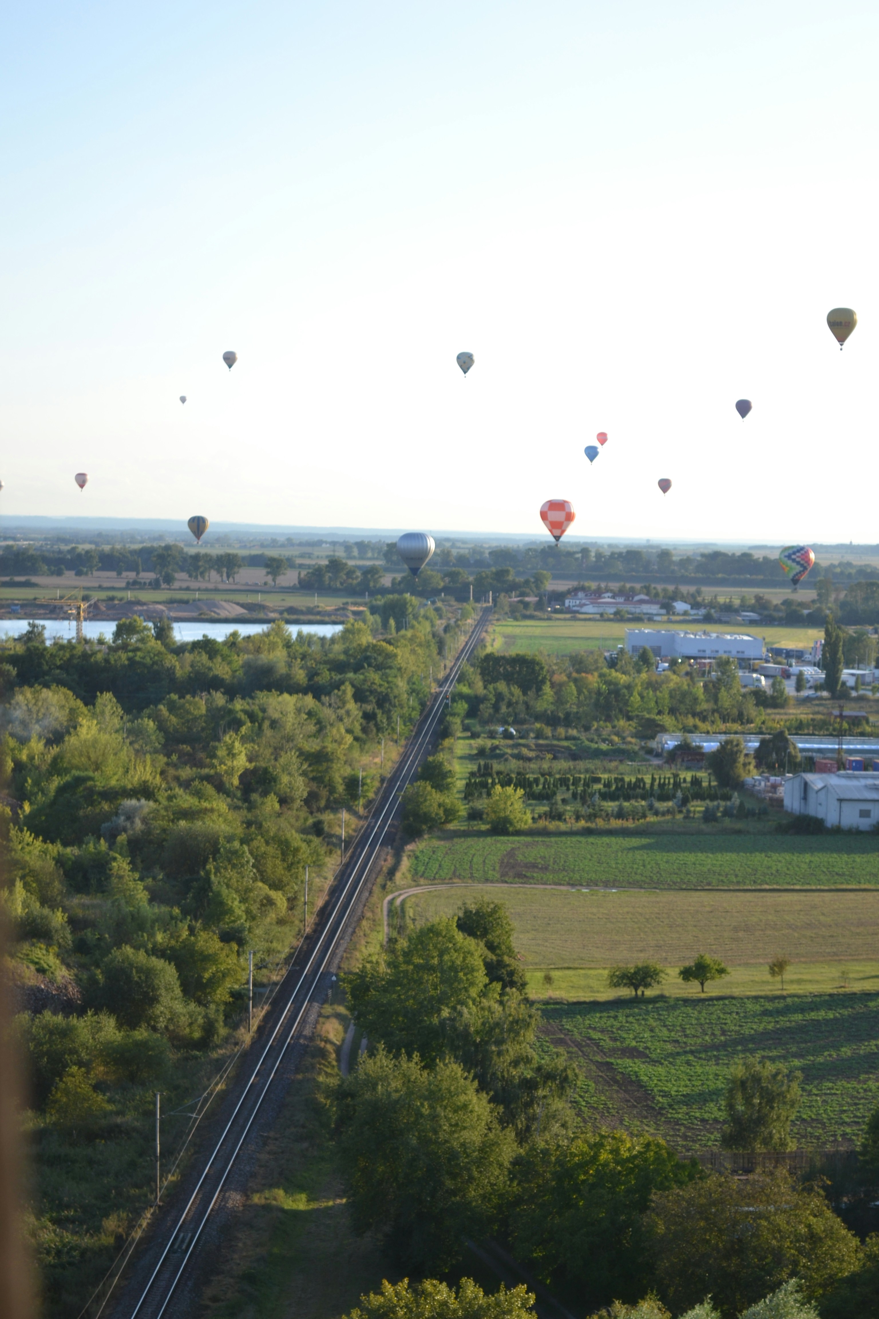 Hot air balloons float over a rural landscape with train tracks.
