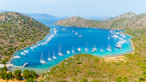 Sailboats anchored in a clear blue bay surrounded by hills