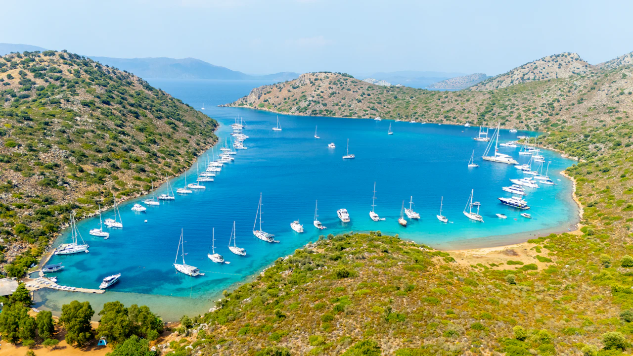 Sailing boats anchored in a clear blue bay surrounded by hills