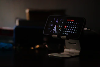 Smartphone displaying clock and calendar on stand.