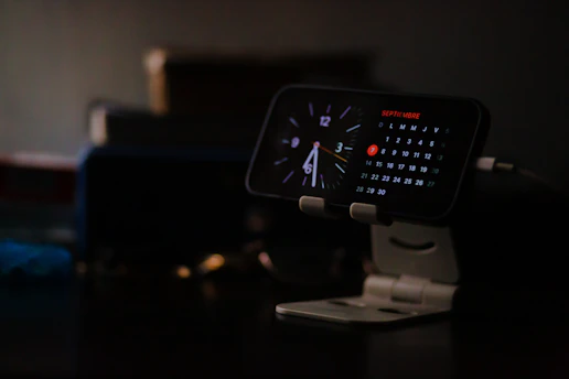 Smartphone displaying clock and calendar on stand.