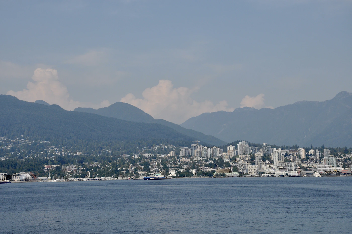 Vancouver downtown skyline with snow-capped Coast Mountains rising directly behind the glass towers, reflected in the harbour