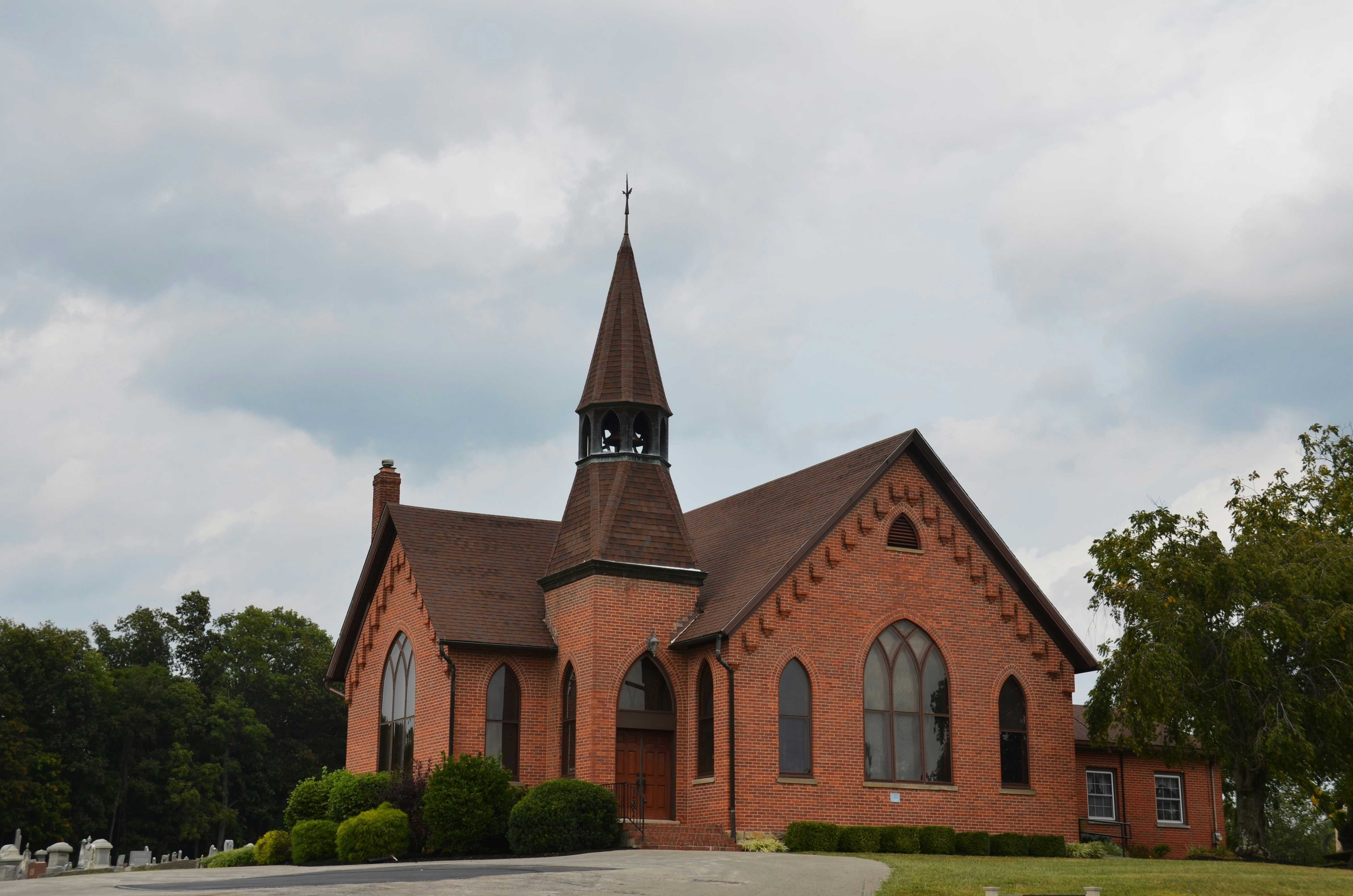 A brick church with a tall steeple under cloudy skies.