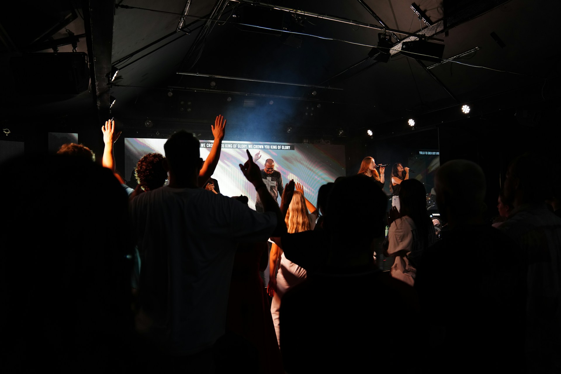 People raising hands in a dark concert venue.