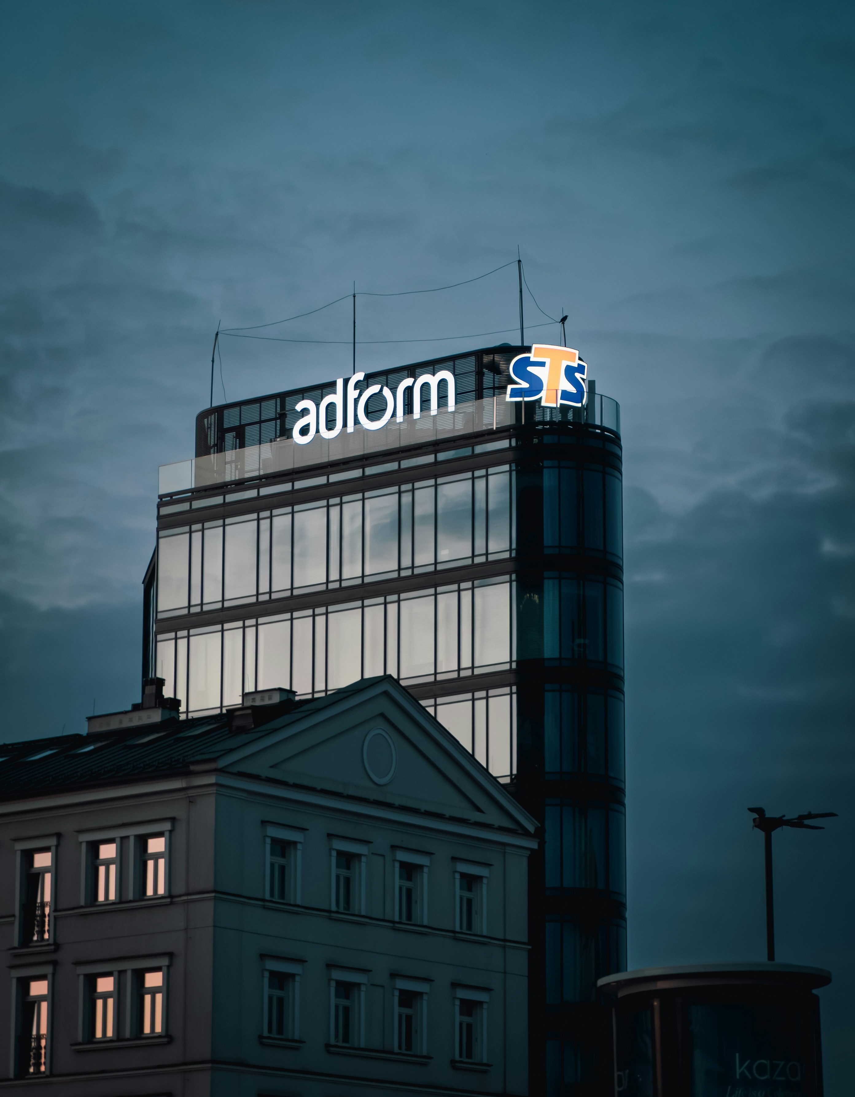 Modernes Glasgebäude mit beleuchtetem Werbeschild in der Dämmerung.