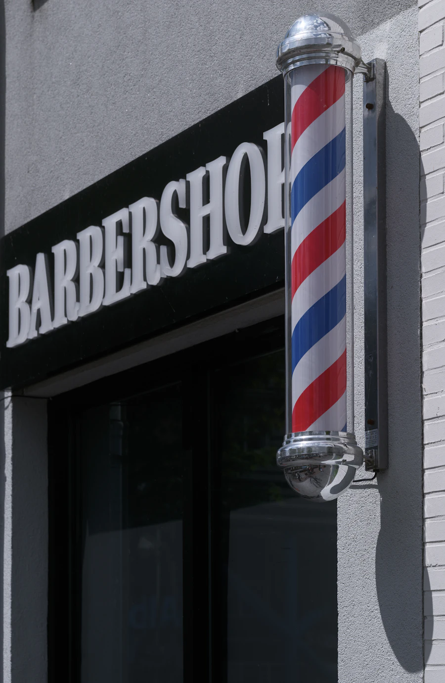 A black barbershop sign and a spinning barber pole outside the shop