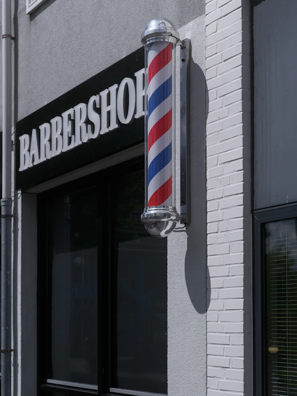 A barbershop sign and a red, white and blue barber pole on a white brick wall