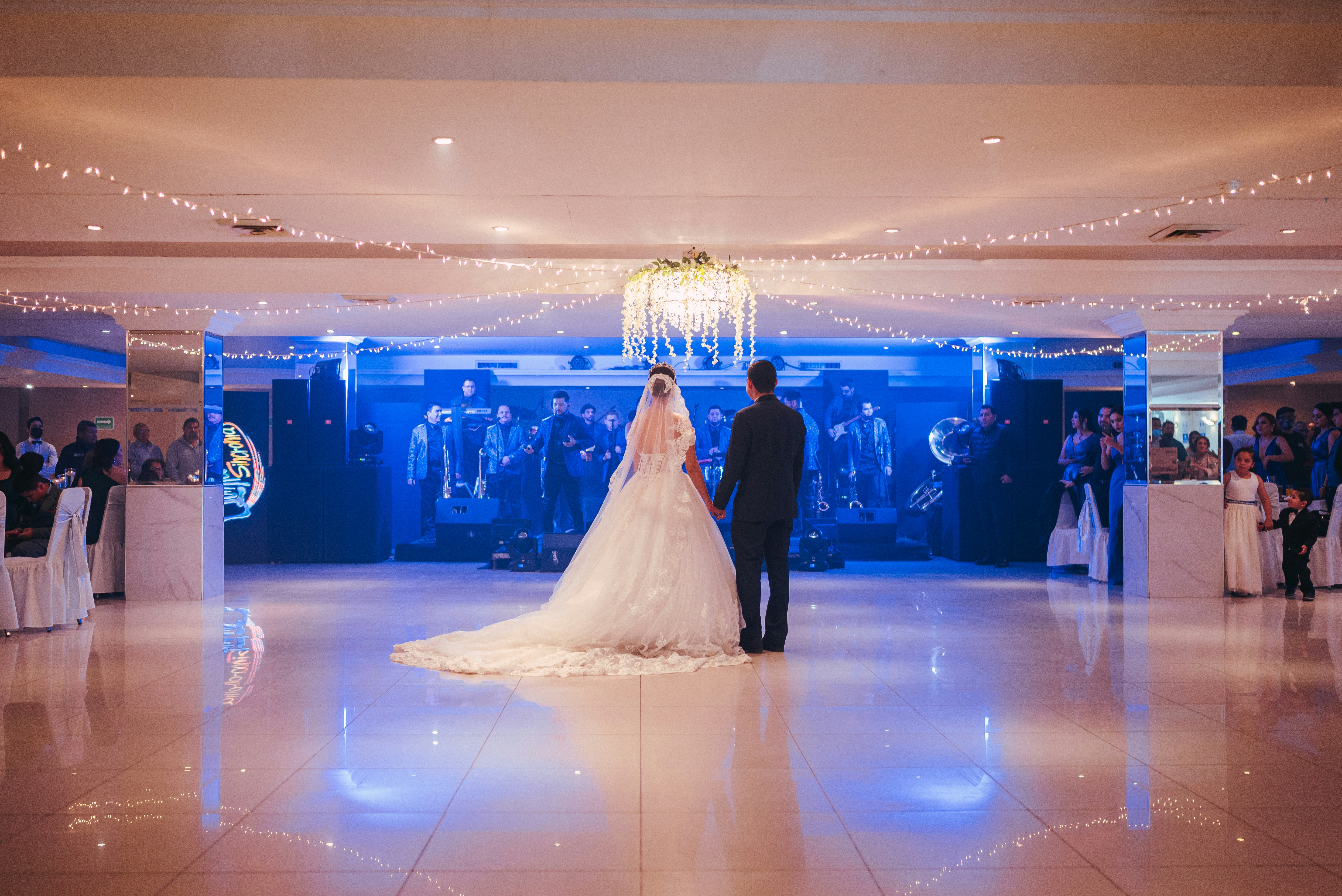 A subtle image of a wedding ceremony from a distance, perhaps showing blurred figures or a decorated room, with a hint of security personnel in the background.