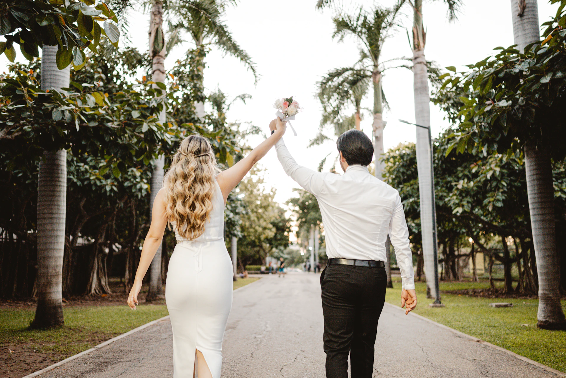 Couple holding hands walking down palm tree lined path