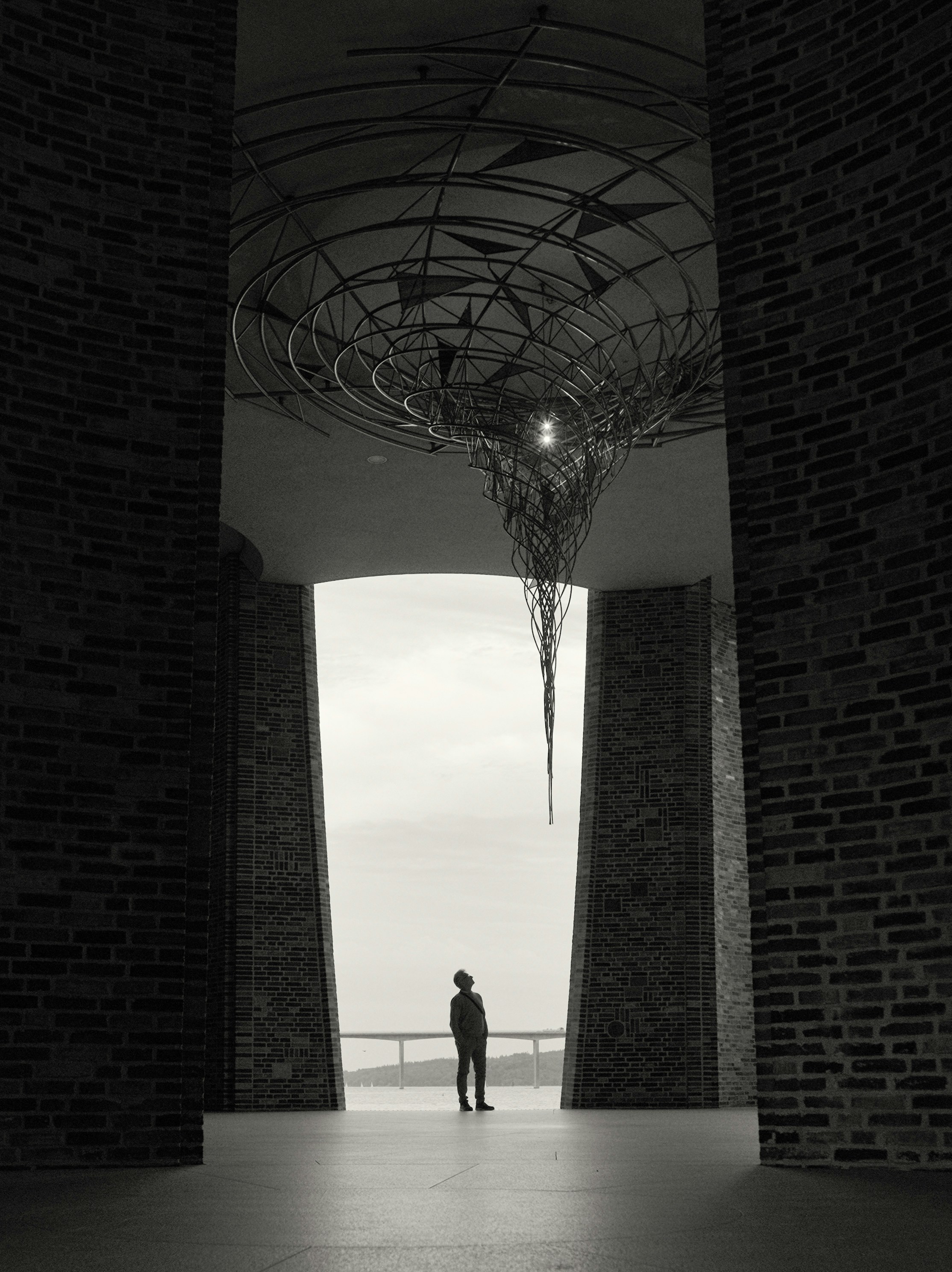 A lone figure stands beneath a large metal sculpture.