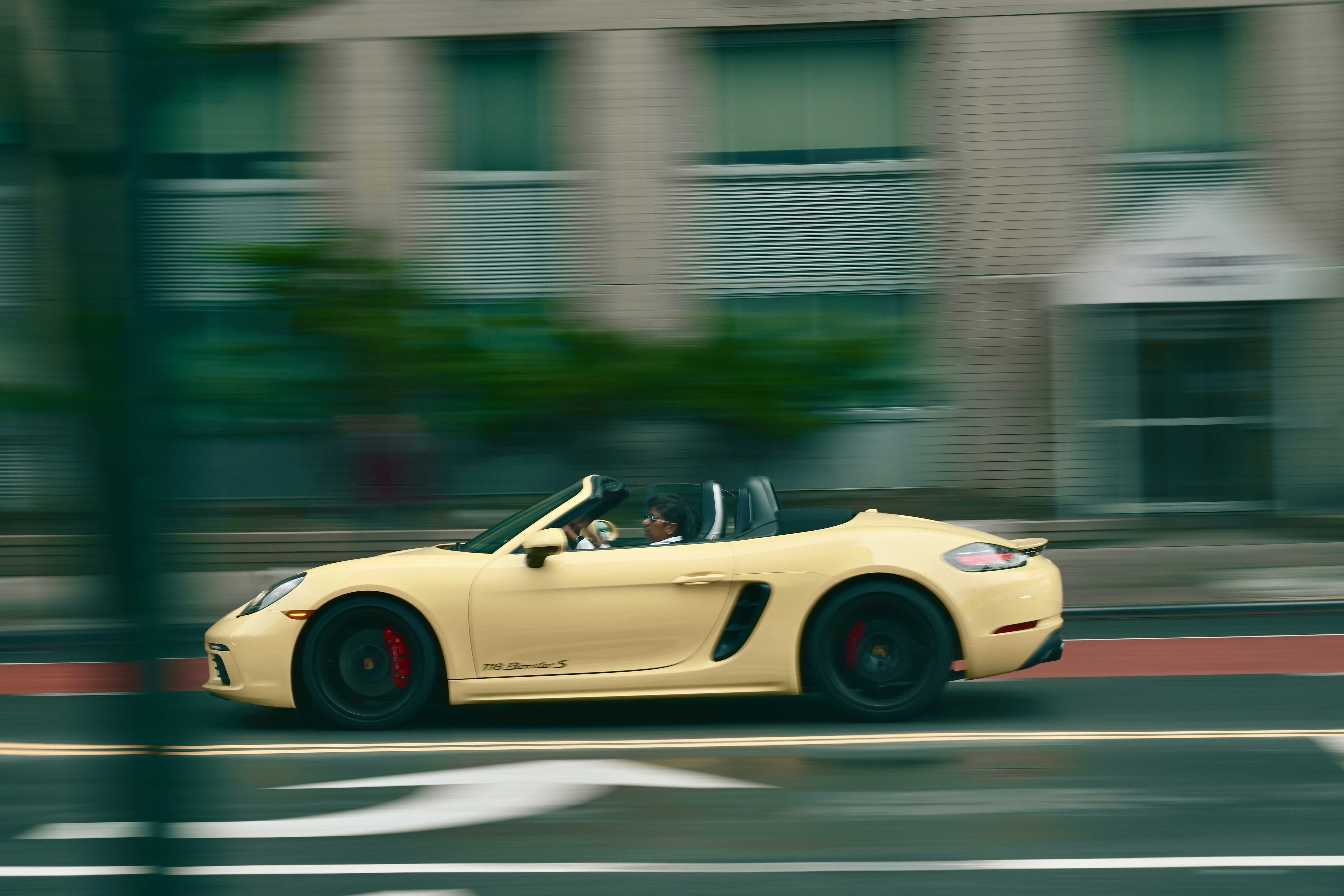 A yellow convertible sports car drives down a street